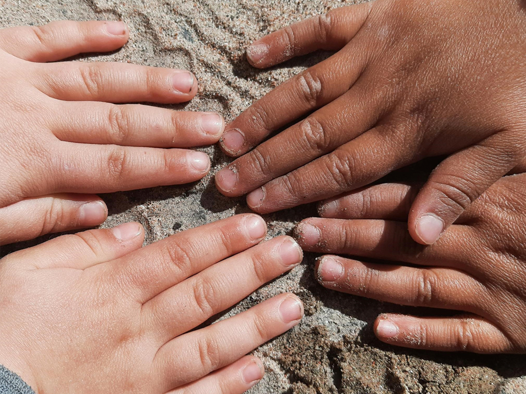 Två barn med händer bredvid varandra i sanden