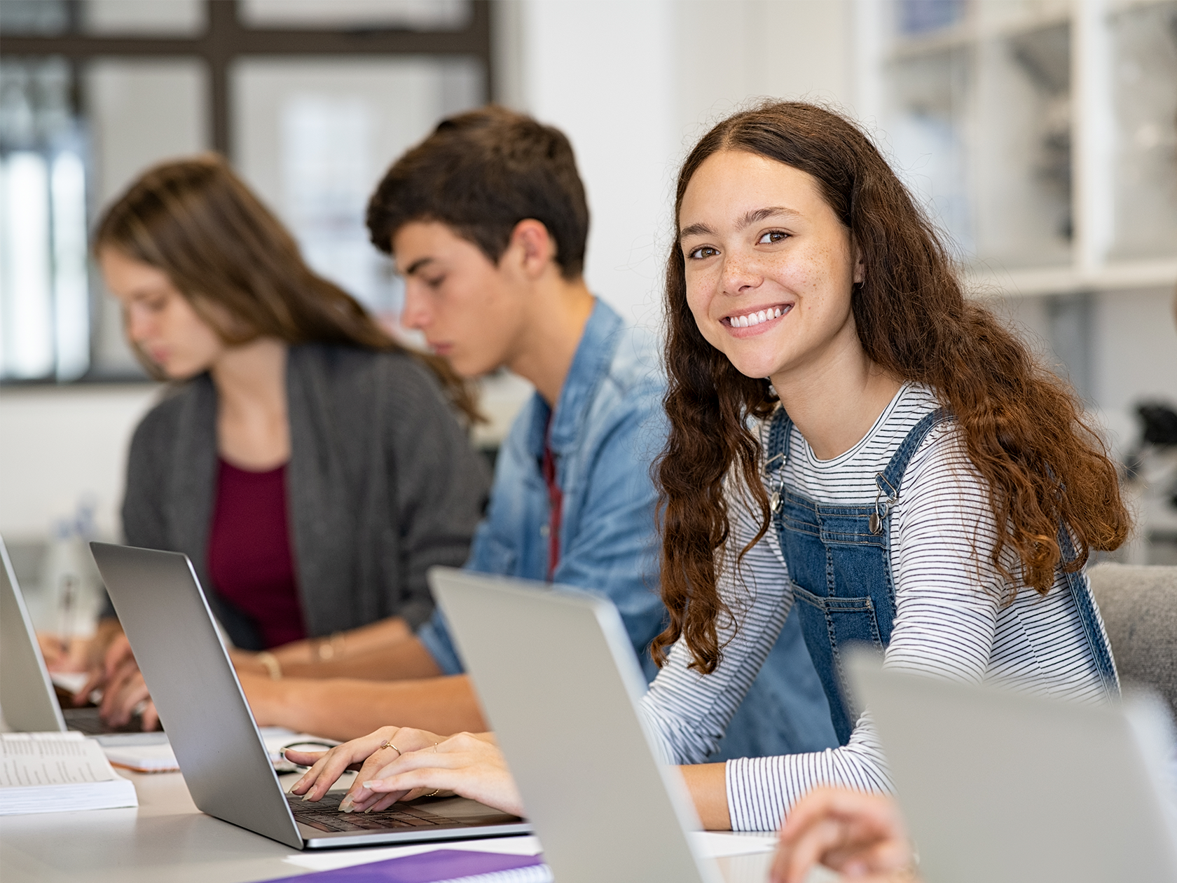 Elev som sitter framför en dator med andra elever och ler