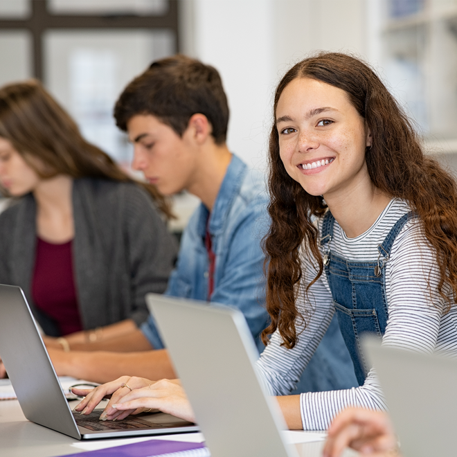 Elev som sitter framför en dator med andra elever och ler
